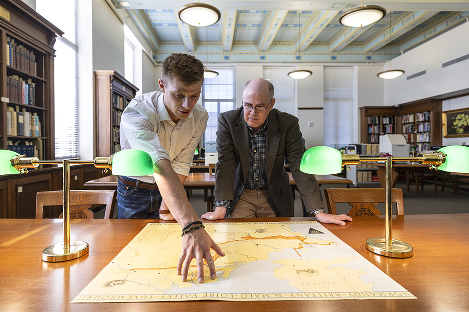 Student and professor examine a map on table in library