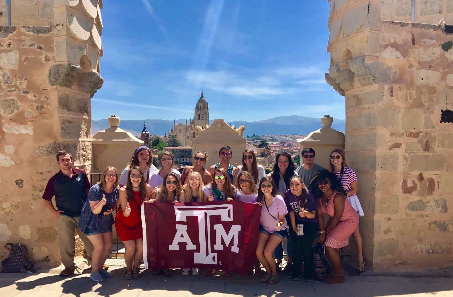 Group of students holding up Texas A&amp;M flag in foreign country