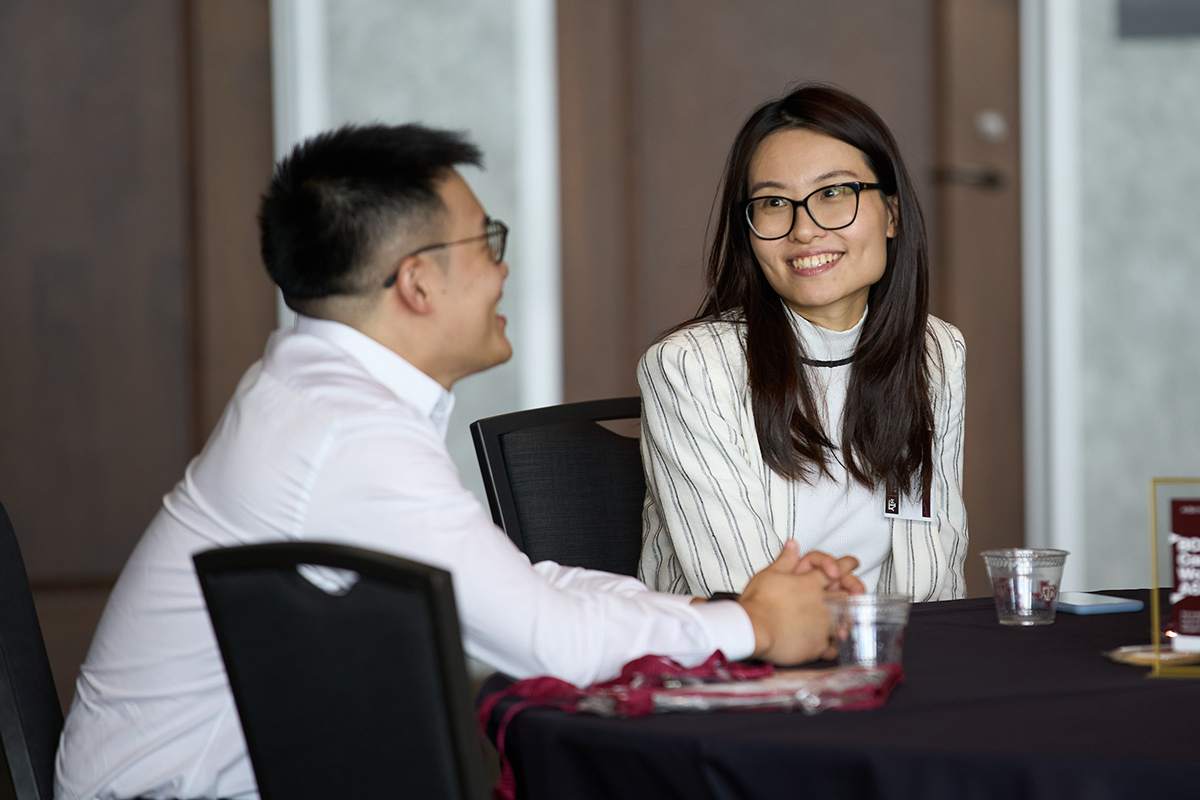 Woman with glasses gives big bright smile to man with glasses while sitting at conference table