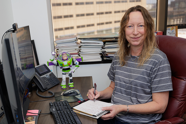Director of Communications, Shana Hutchins '93 sitting at desk next to Buzz Lightyear Figure
