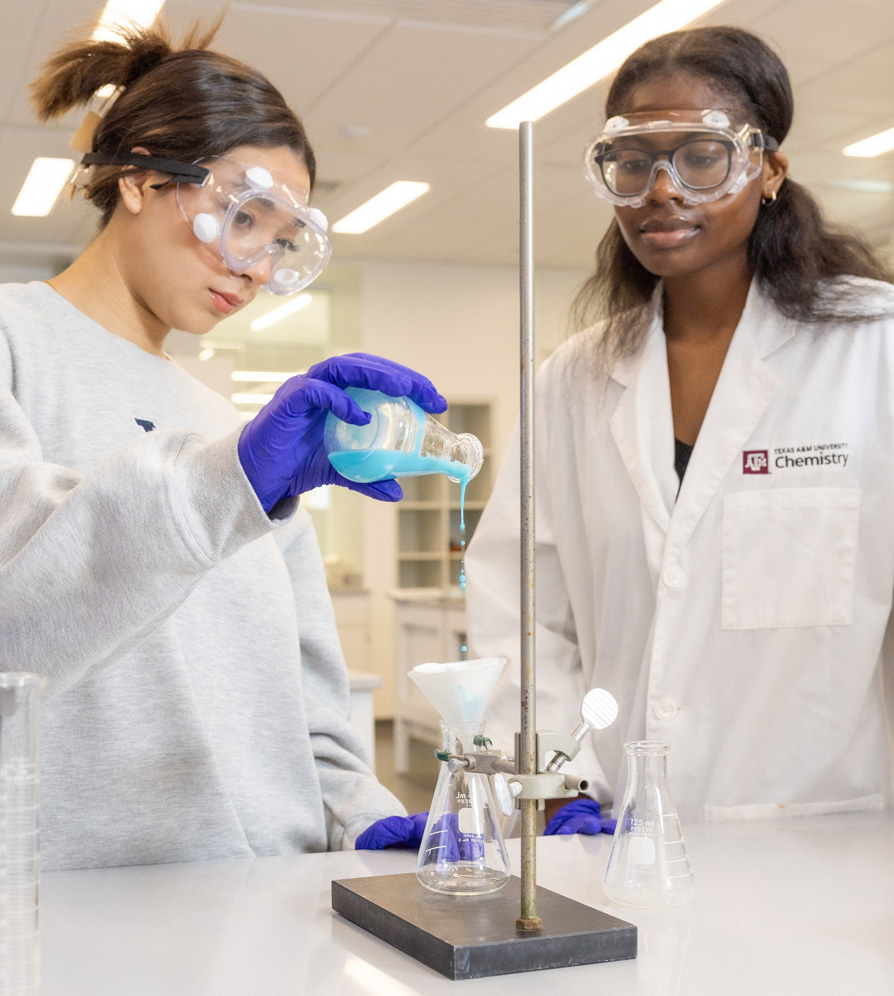 two students pouring chemicals in lab experiment