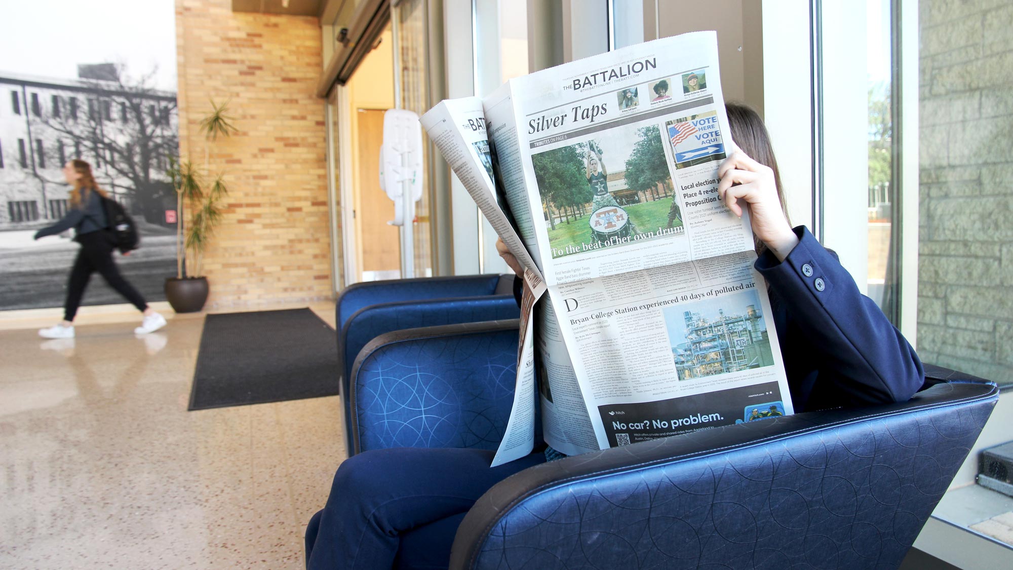 A person sitting in a chair at the MSC and reading the Battalion newspaper