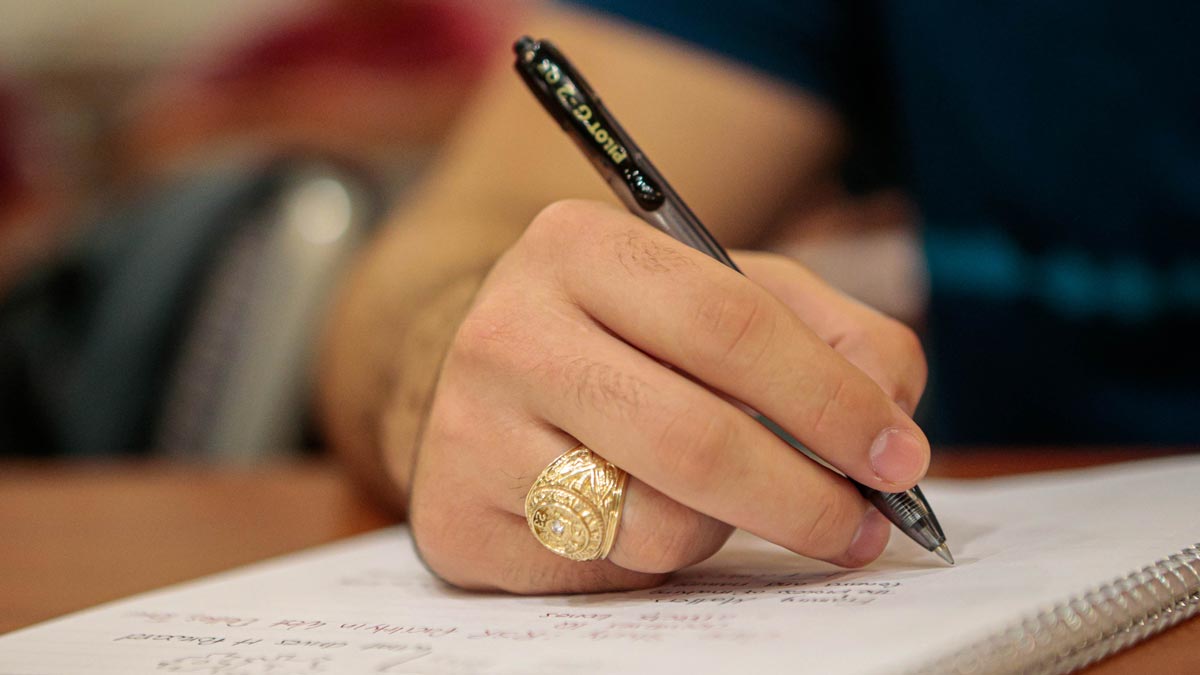 Close up view of a student taking notes with a black ballpoint pen, focused on their Aggie Ring
