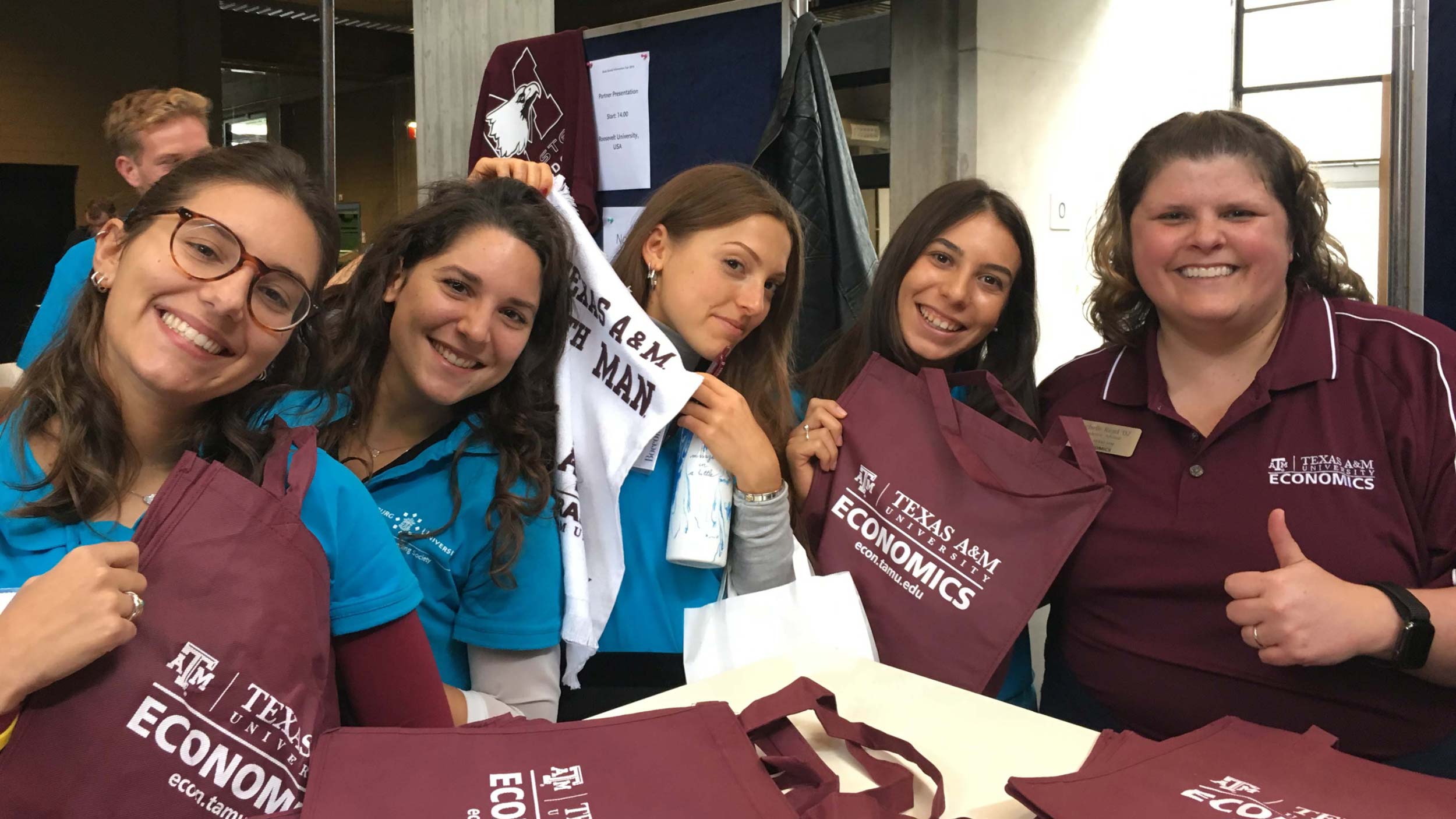 Five economics students pose with their department swag, such as tote bags and 12th man towels