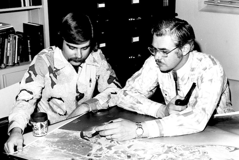 two men sitting at table looking at map