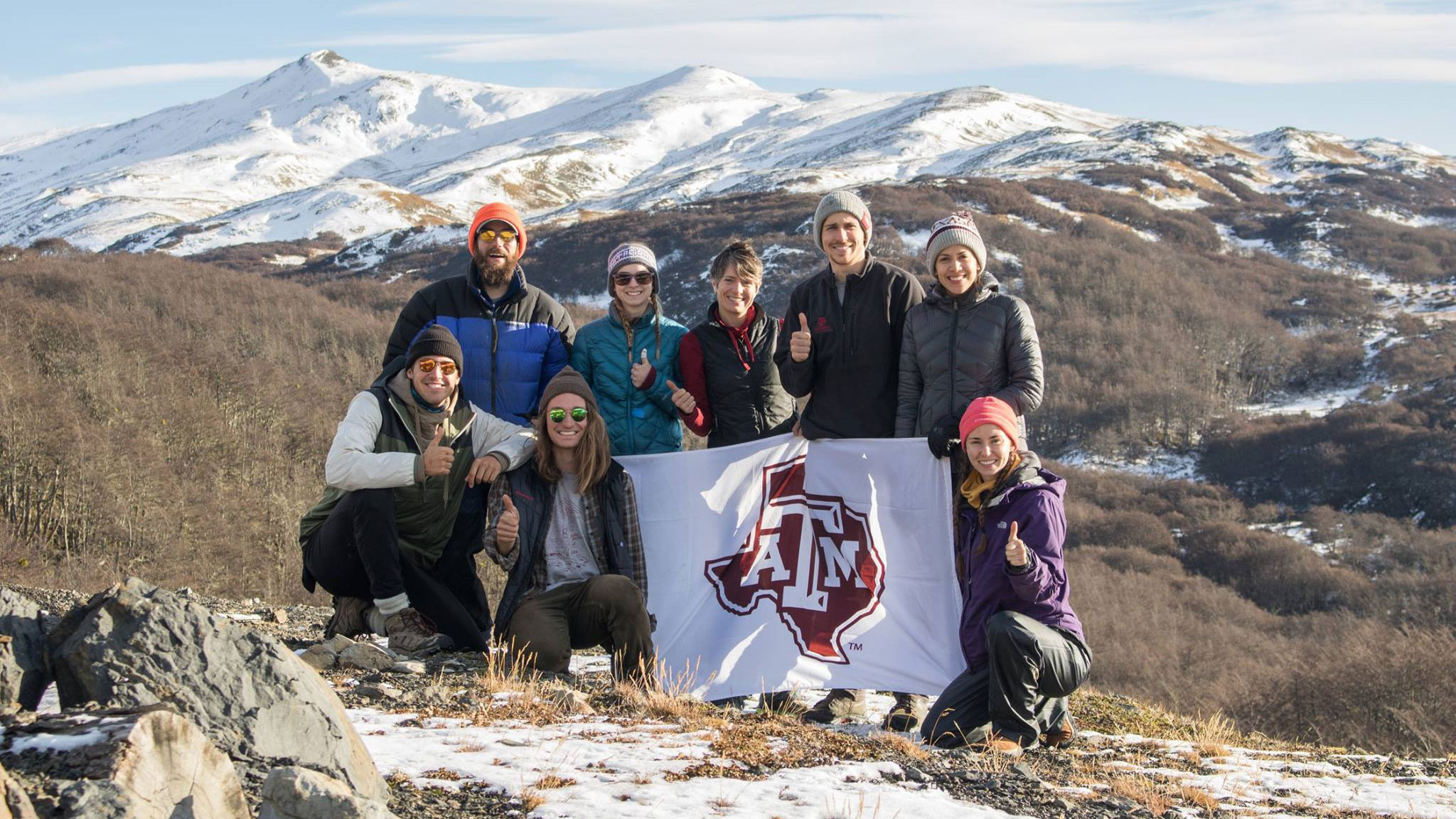 Group of students holding a Texas A&amp;M flag in front of snow covered mountains