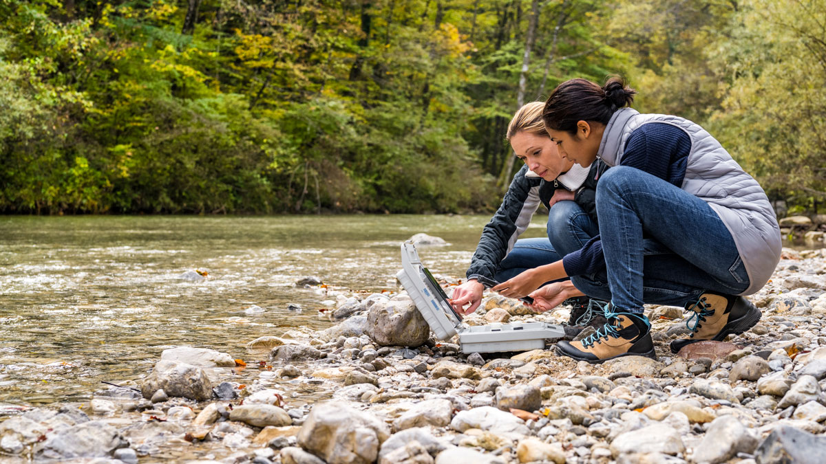 Two female students on the shore of a river taking measurements for research