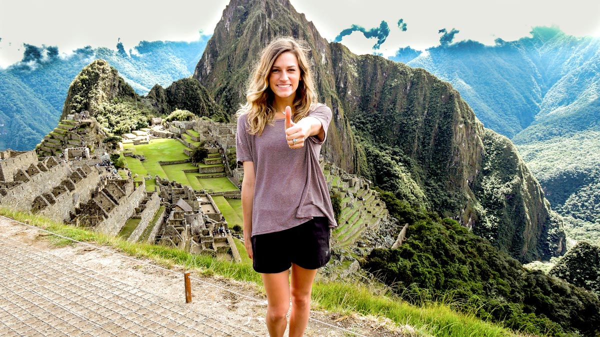 Female student giving a "gig 'em" gesture in front of scenic mountains