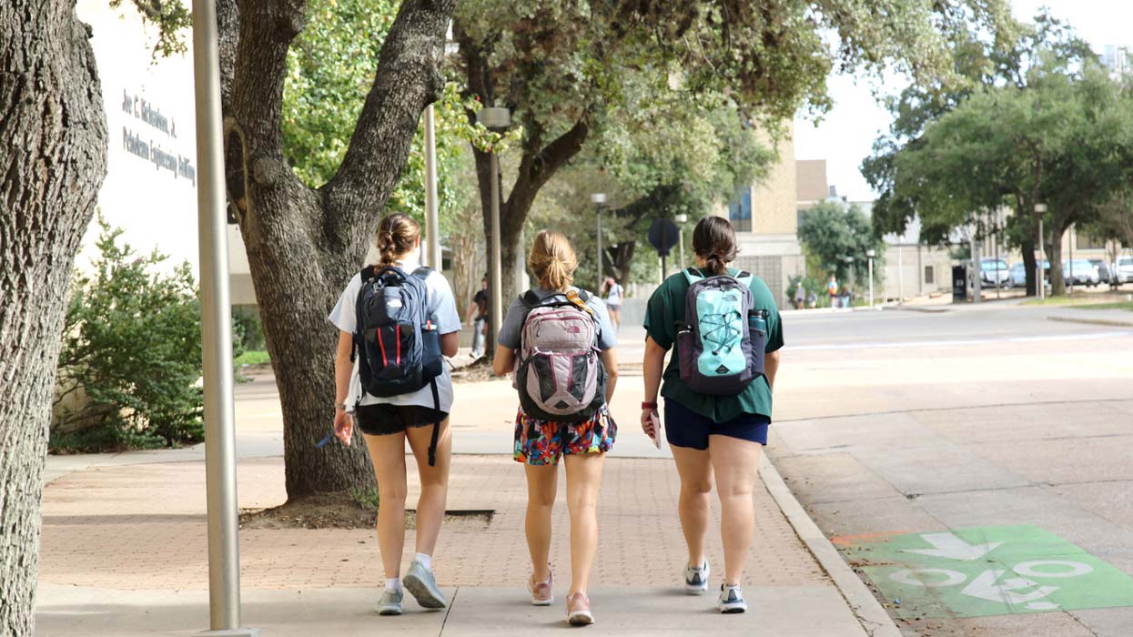Three students with backpacks walking down the sidewalk