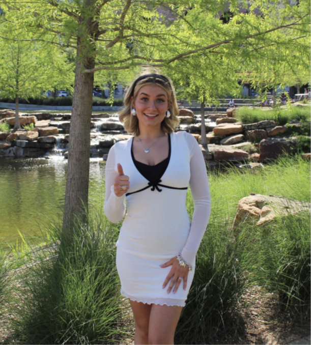 young caucasian woman wearing white dress stands outdoors with a thumbs up pose
