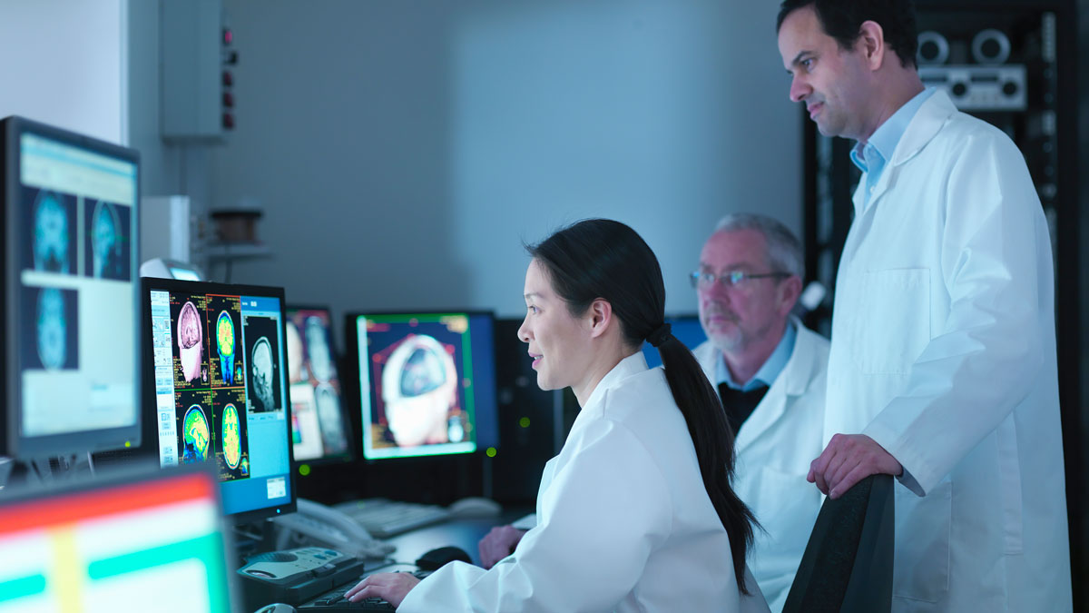 Three medical professionals looking over various scans and activity maps of the brain.
