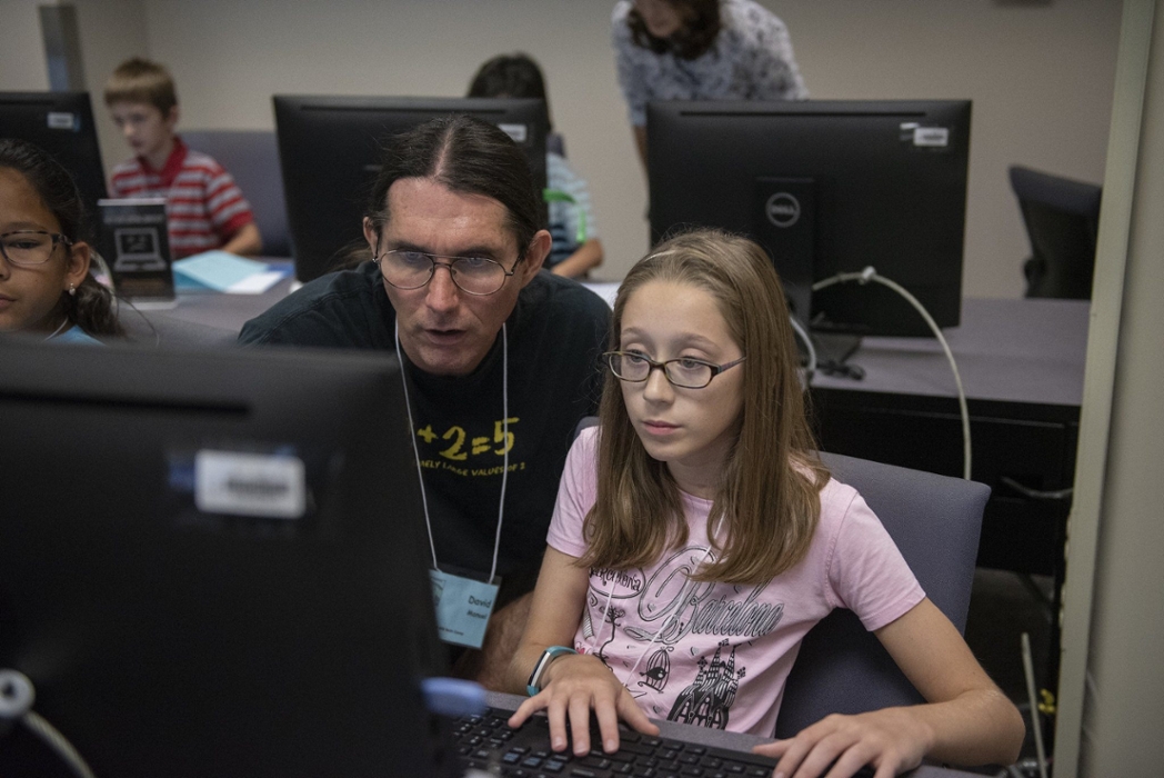 A man assists a young girl as they both stare at a computer screen.