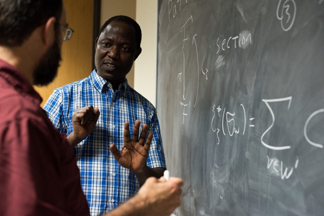 Two mathematics professors discuss and solve an equation written on a chalkboard.