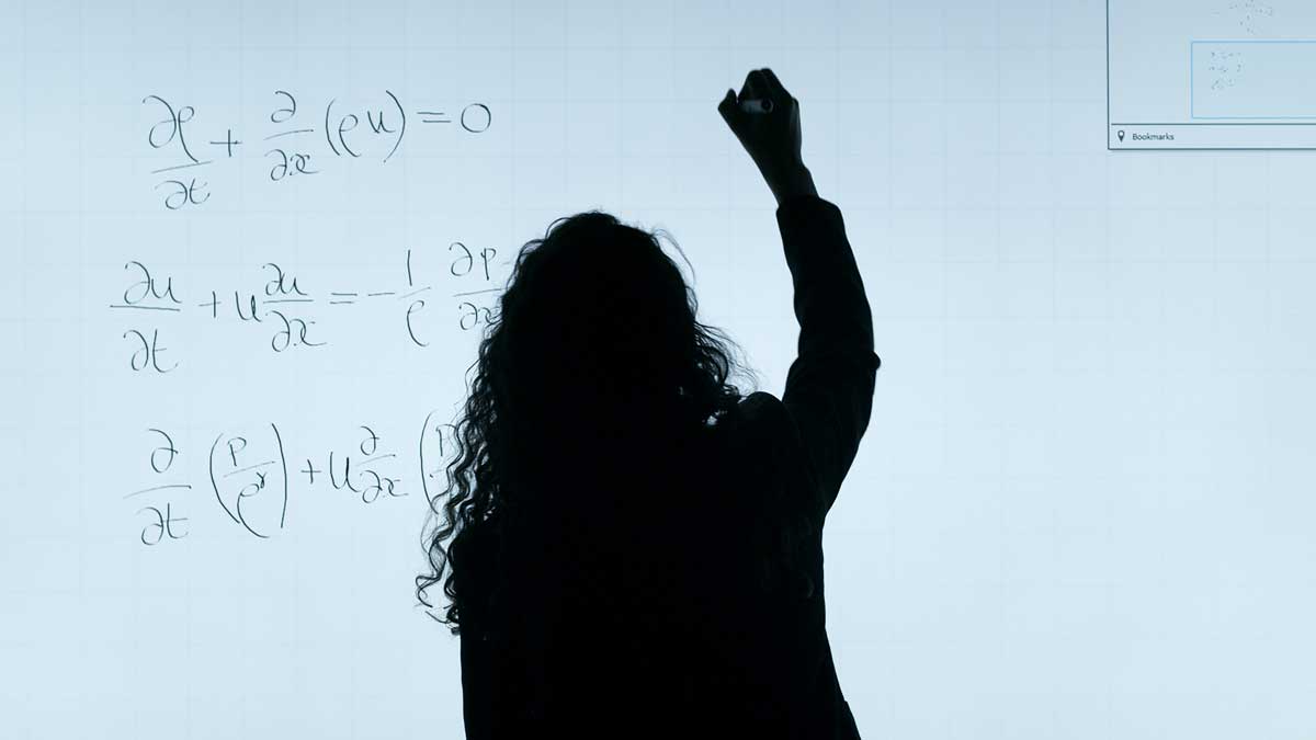 Silhouette of a woman writing on a board several complicated math equations.