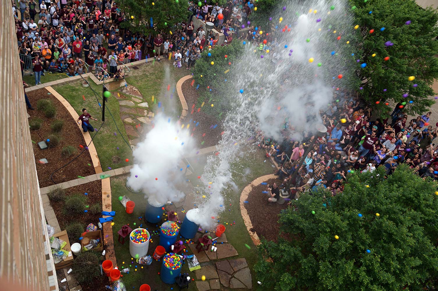 Aerial of colored balloons and water exploding while hundreds of people look on