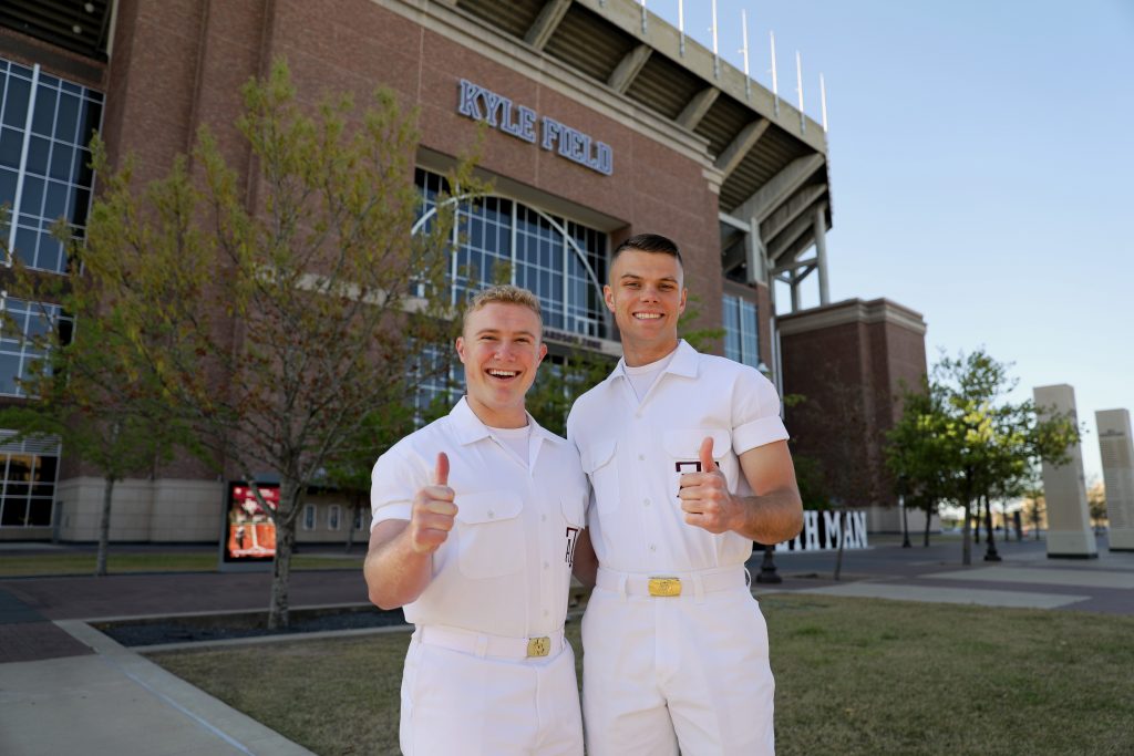 Two yell leaders, posing with thumbs up in front of Kyle Field 