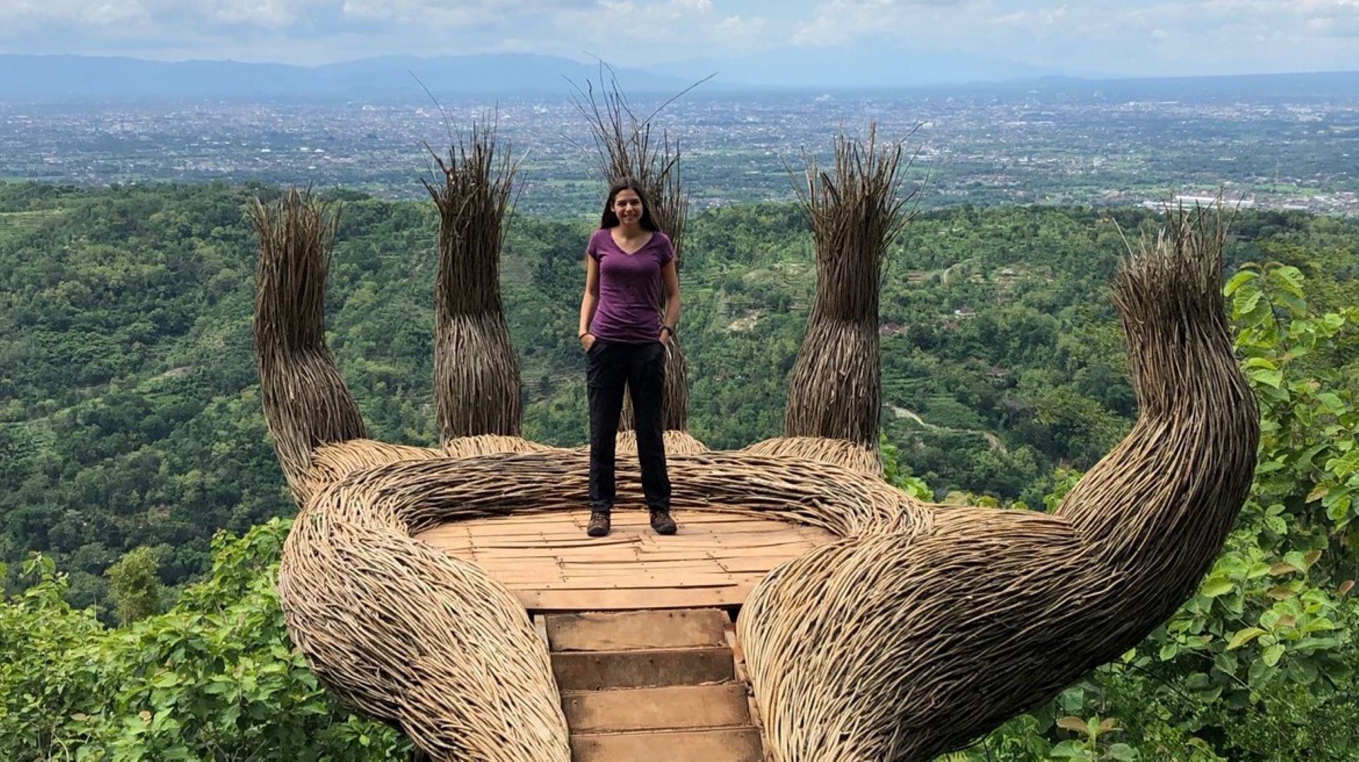 Doctoral student Angela Achorn stands in the middle of a woven wooden structure overlooking an expanse of trees.