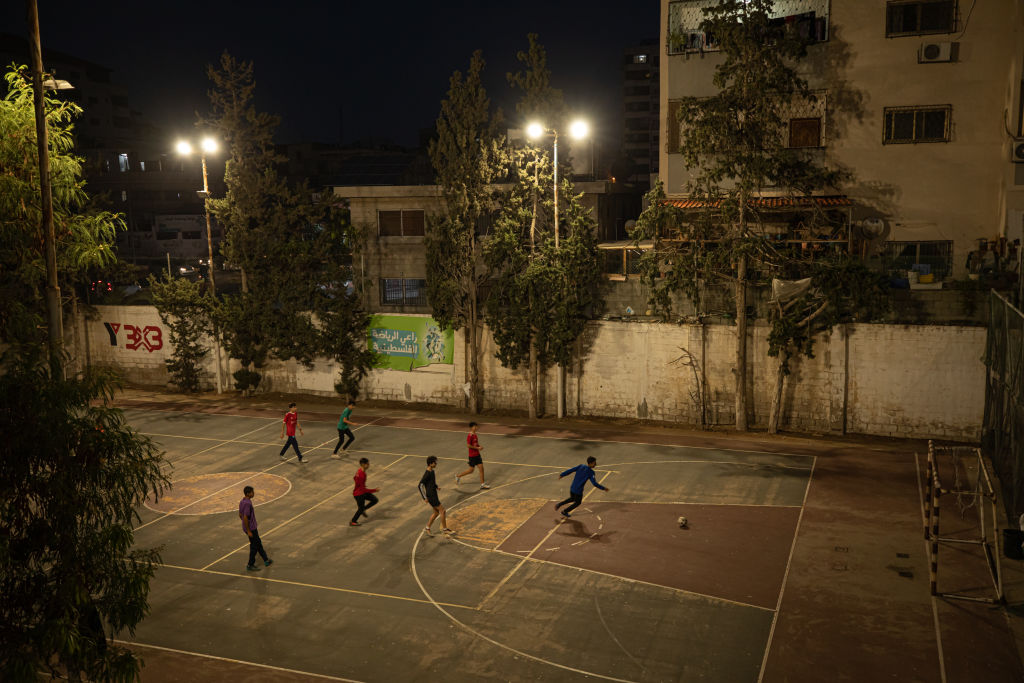 Youth playing soccer at night on an outdoor basketball court under street lighting