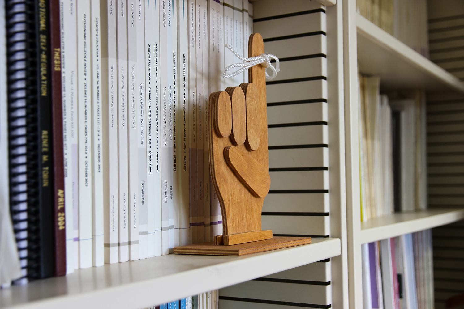 Wooden figurine of a hand on a bookshelf featuring a white string tied around the upward-pointing index finger to signify memory