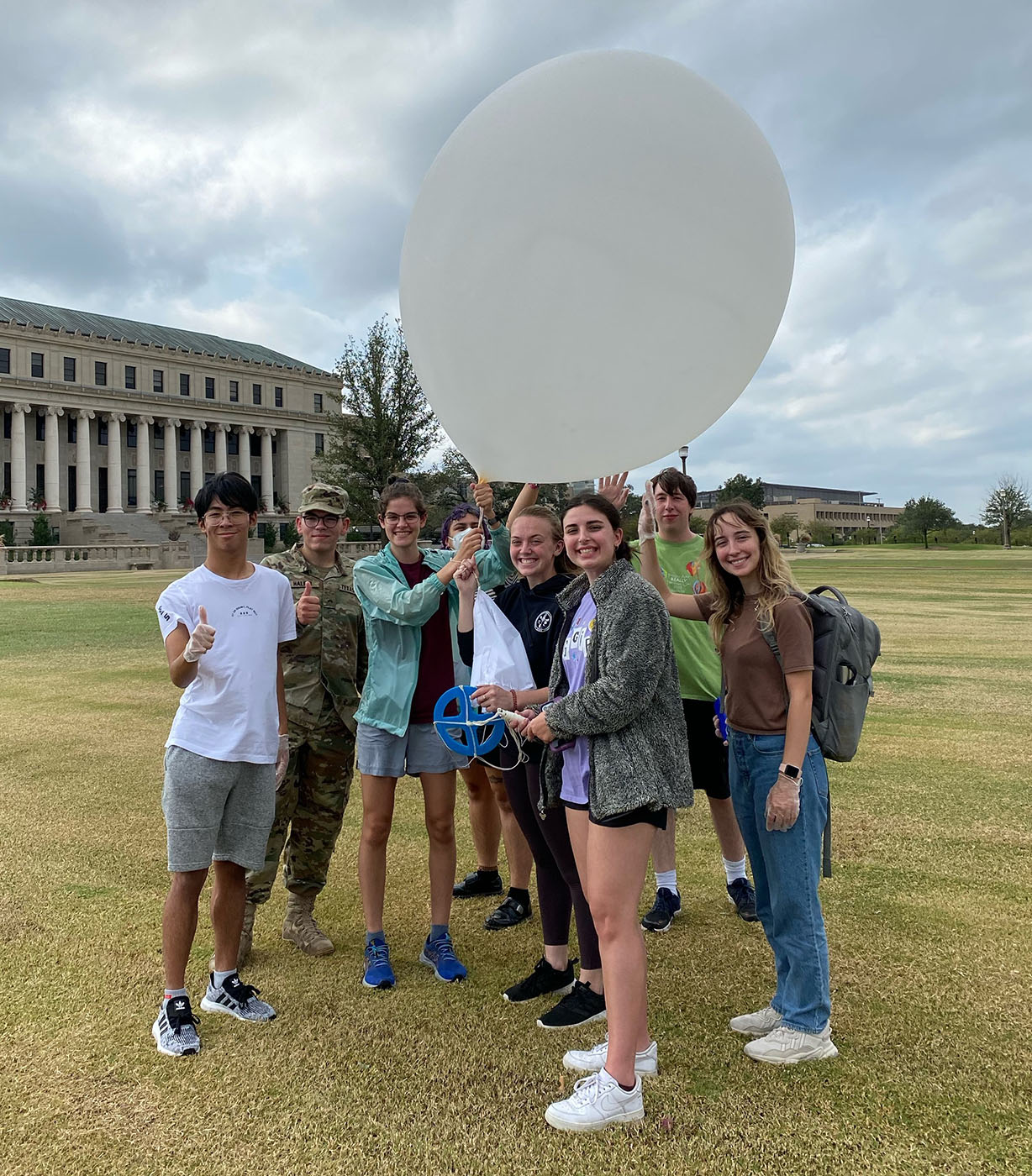 Atmospheric Sciences students pose for a photo, with a large white weather balloon, in front of the Administration Building on the Texas A&M campus before launching a weather balloon.