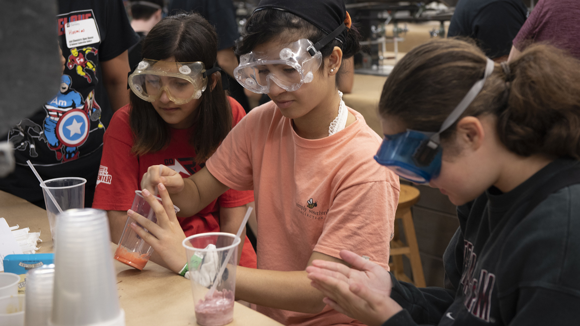 three female students with goggles on in preforming laboratory experiment