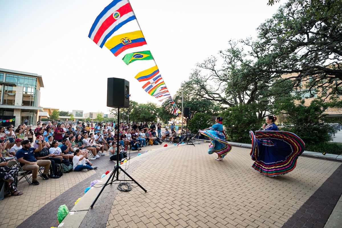 Dancers dressed in brightly colored traditional dresses show off their skills in front of a large crowd at Rudder Plaza on the Texas A&amp;M University campus