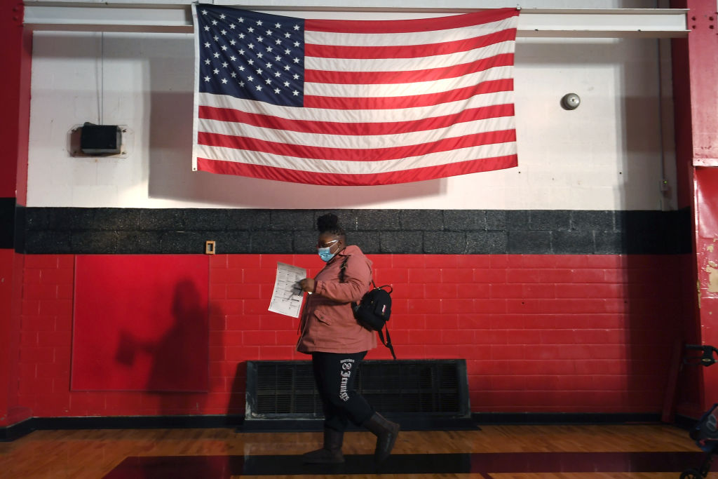 A woman carrying her printed ballot walks down a hallway with an American flag hanging on the wall in the background