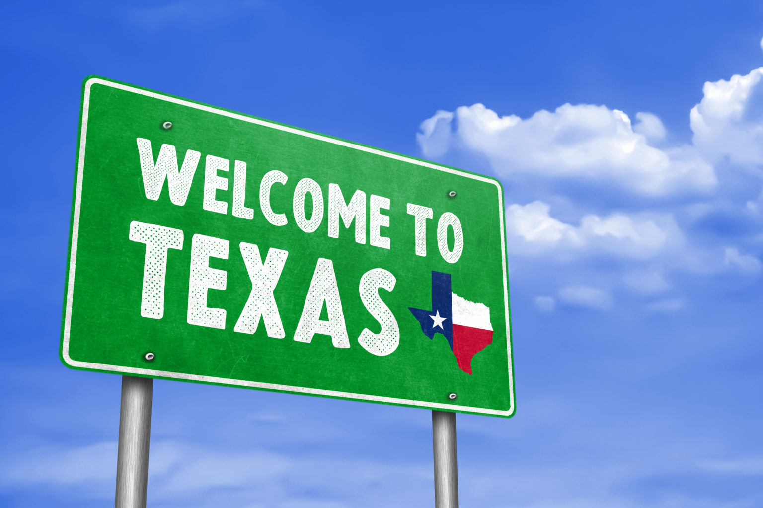 Green billboard against a backdrop of a blue sky with sparse white clouds stating "Welcome To Texas" in white text along with a state of Texas outline featuring the state flag in red, white and blue along with a white star