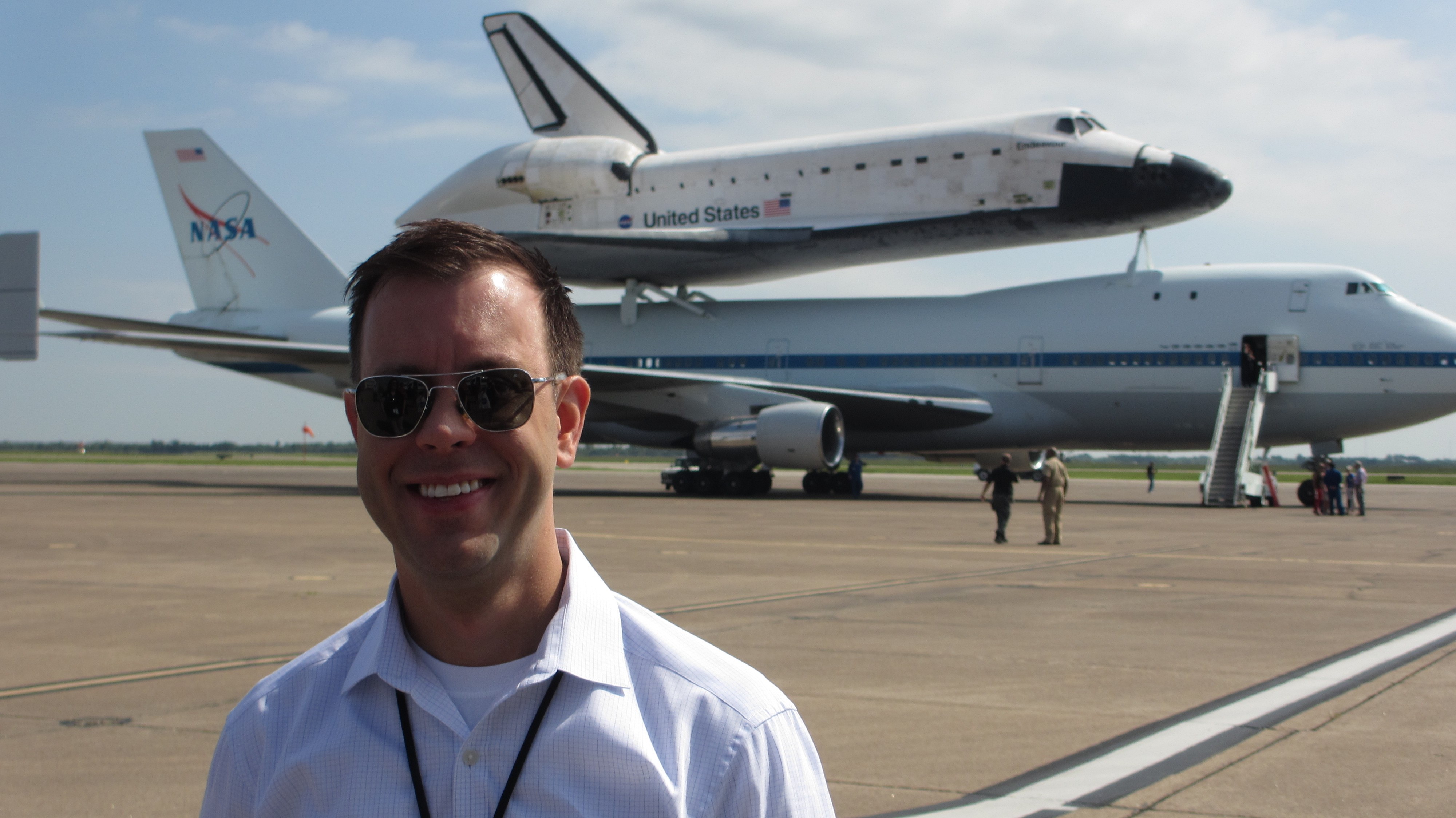1999 Texas A&amp;M journalism graduate Josh Byerly stands on the tarmac with the Space Shuttle Endeavour atop a NASA Shuttle Carrier Aircraft in the background