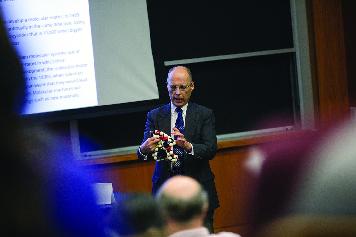 Texas A&M chemist John Gladysz holds a 3-D DNA model while he lectures to a full auditorium
