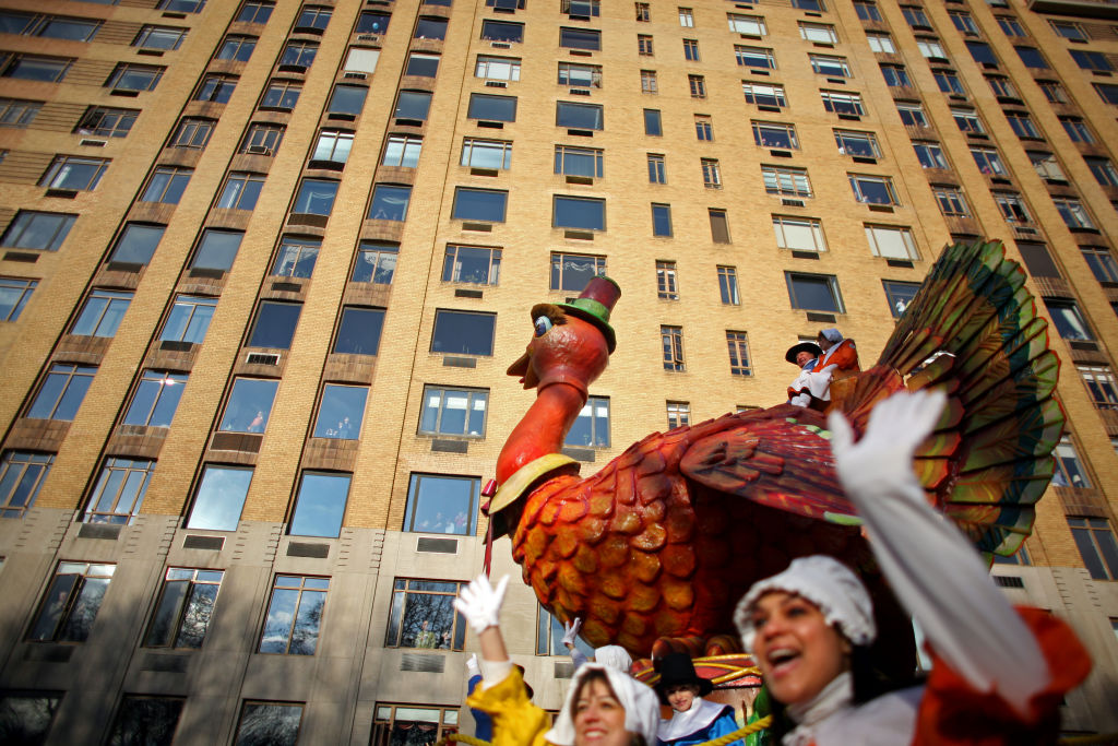 Two women dressed in Pilgrim attire wave with a giant turkey float in the background