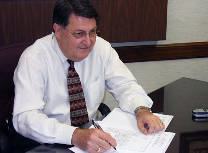 Texas A&amp;M mathematician Richard Ewing smiles as he looks up from his paperwork with pen in hand.