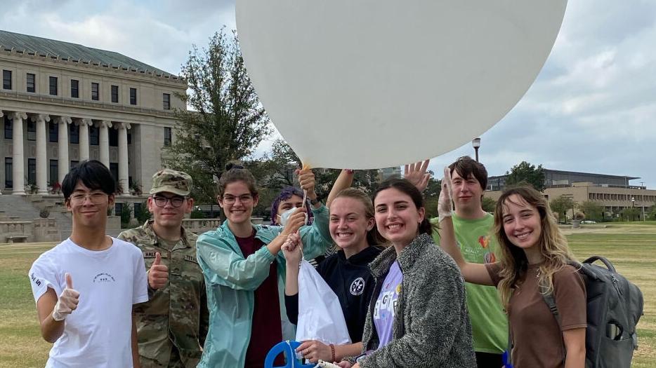 Atmospheric Sciences students pose for a photo, with a large white weather balloon, in front of the Administration Building on the Texas A&M campus before launching a weather balloon.