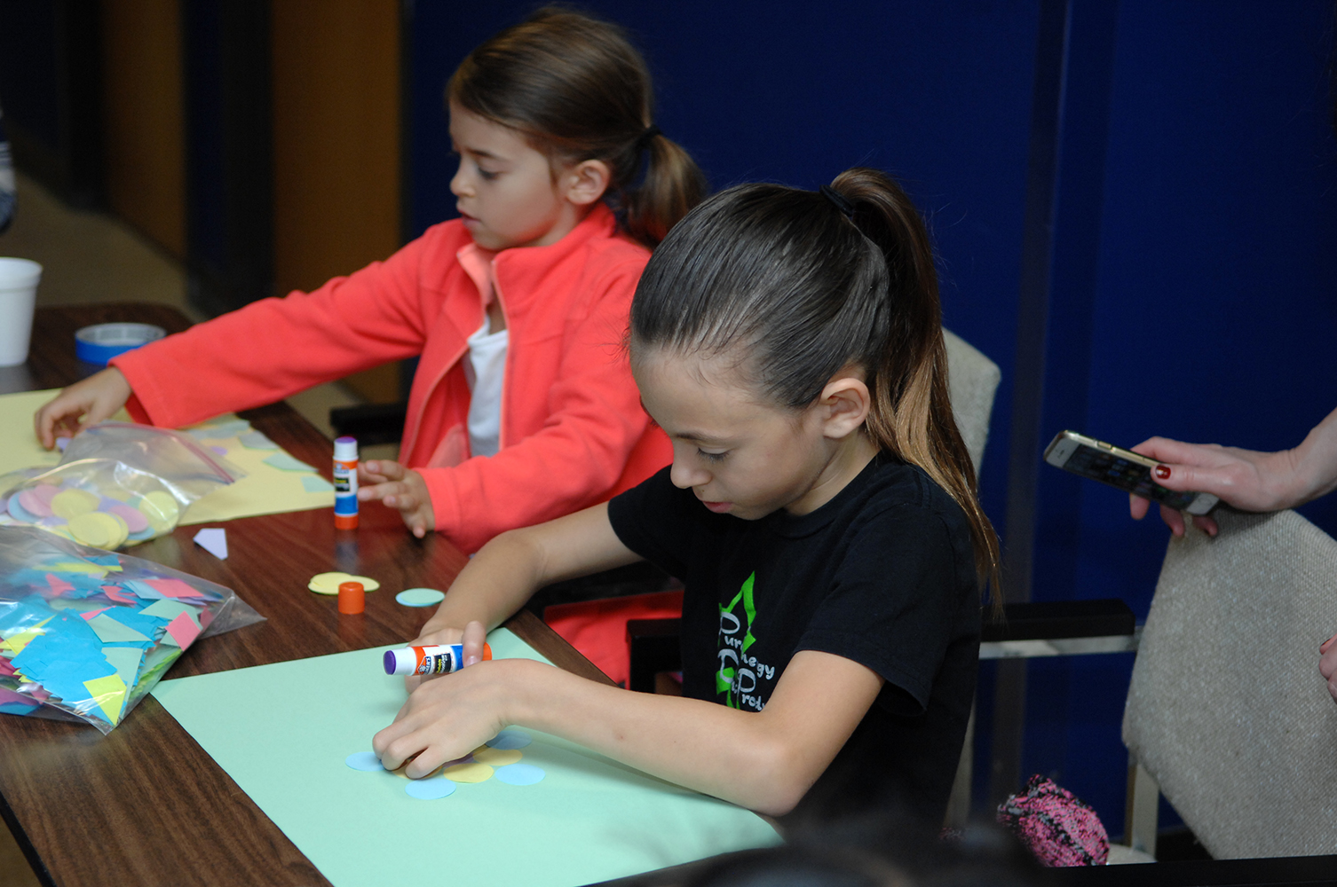 Two young girls use glue sticks and construction paper at the Math and Stat Fair