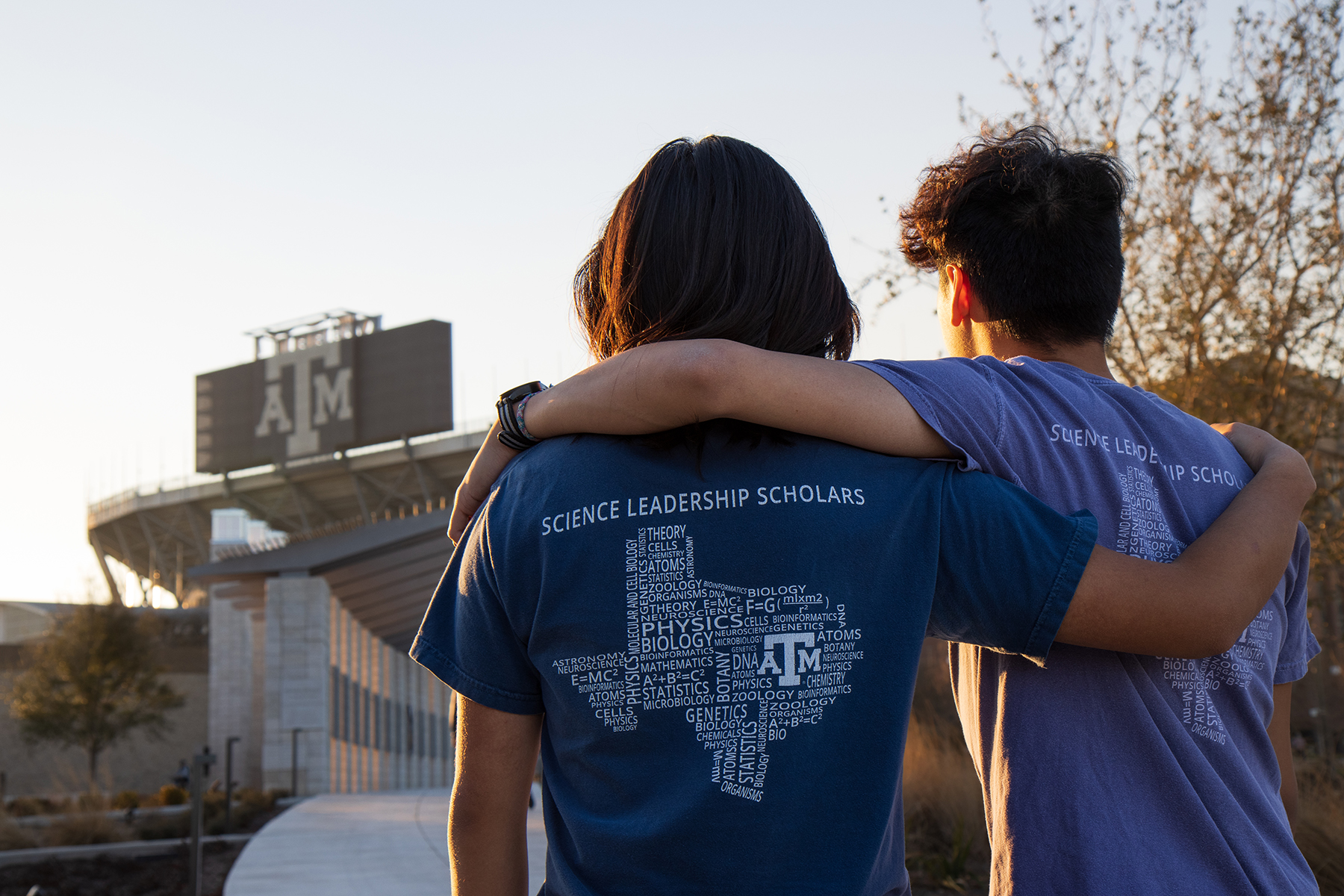 Texas A&amp;M biology majors and brothers Henry and Kyle Nguyen stand arm in arm with their backs to the camera looking toward Kyle Field on the Texas A&amp;M campus