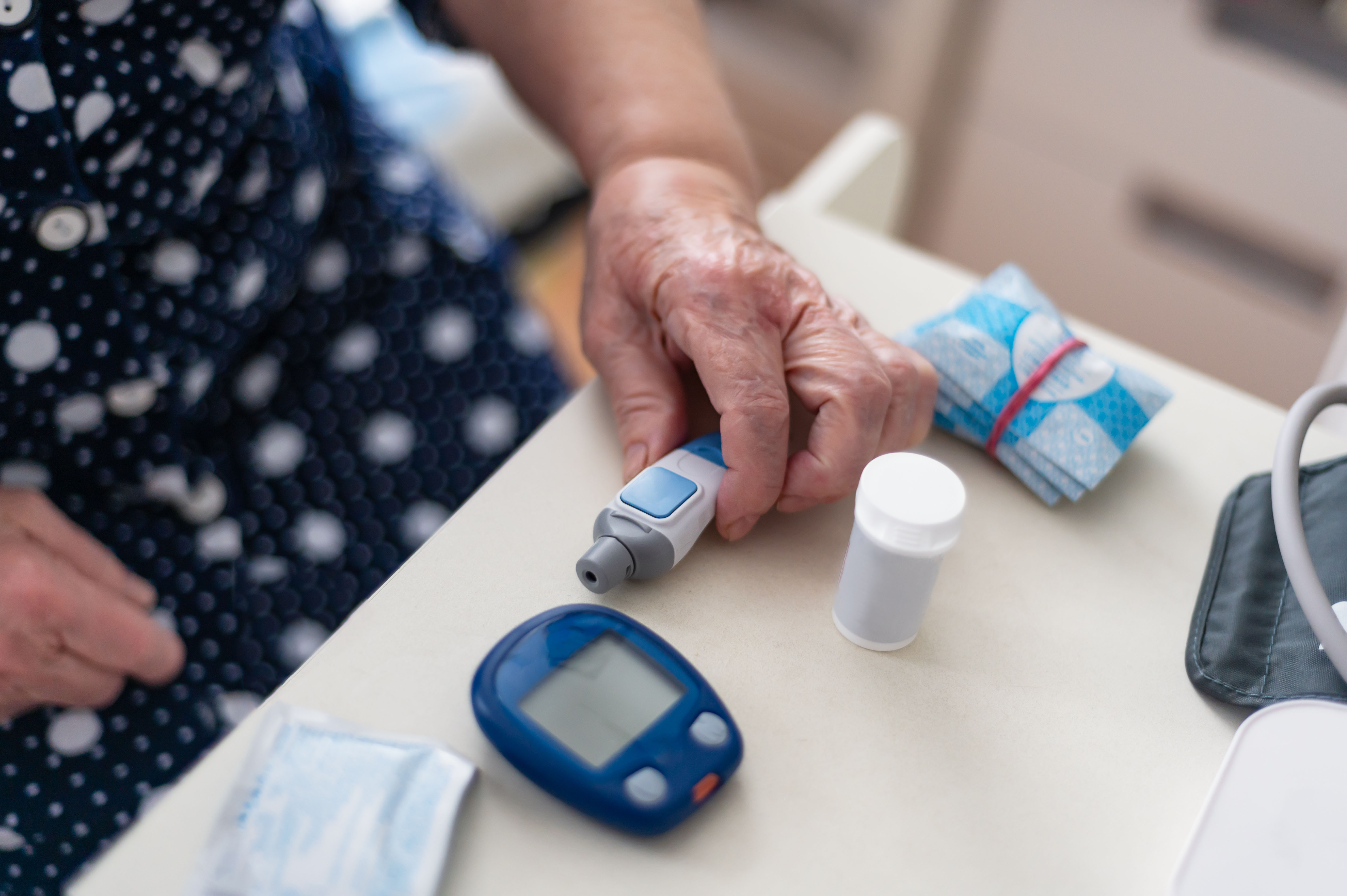 A senior woman tests her blood for glucose or sugar levels for diabetes with a glucometer