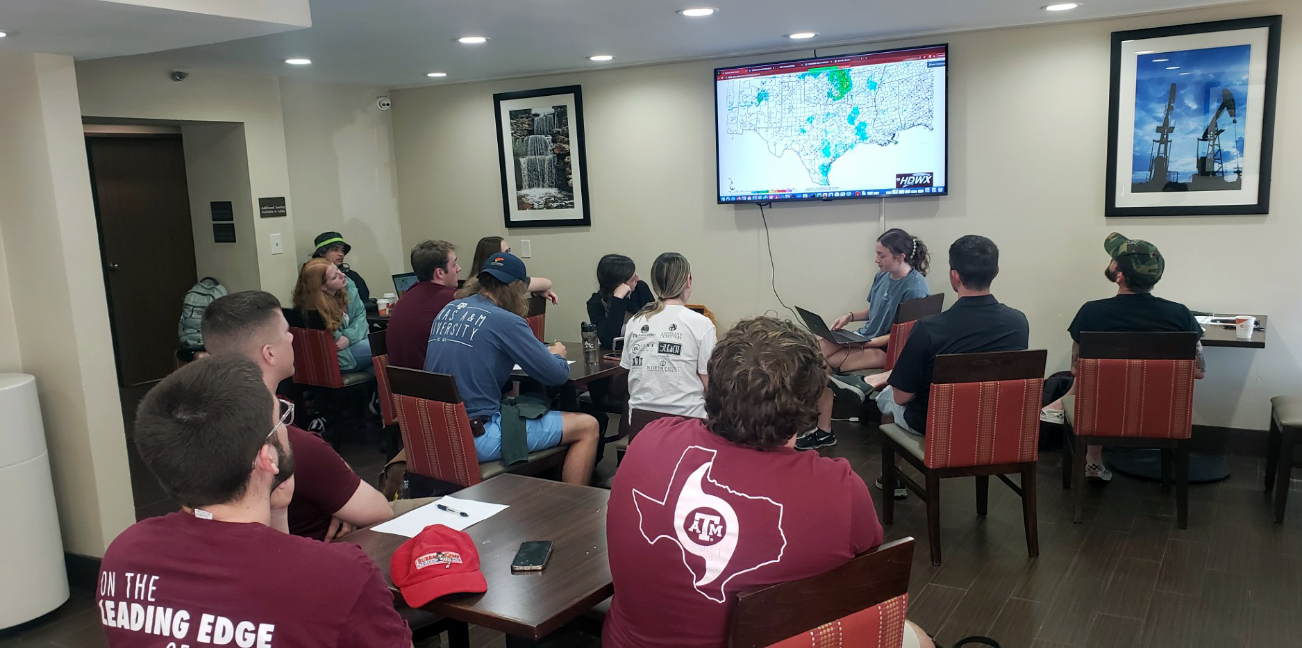Texas A&amp;M meteorology major Bailey Kropp sits with a laptop at the front of a group of seated students while leading a morning weather forecasting briefing in a hotel breakfast room in Wichita Falls, Texas