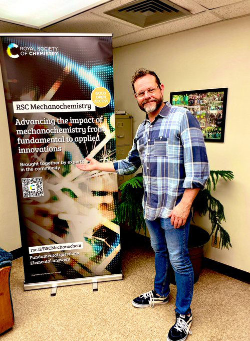 Texas A&amp;M chemist James Batteas stands next to a pull-up banner promoting the new Royal Society of Chemistry journal RSC Mechanochemistry