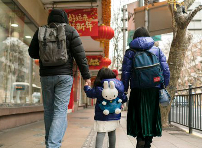 A Chinese couple walks hand in hand with their female child down a city street