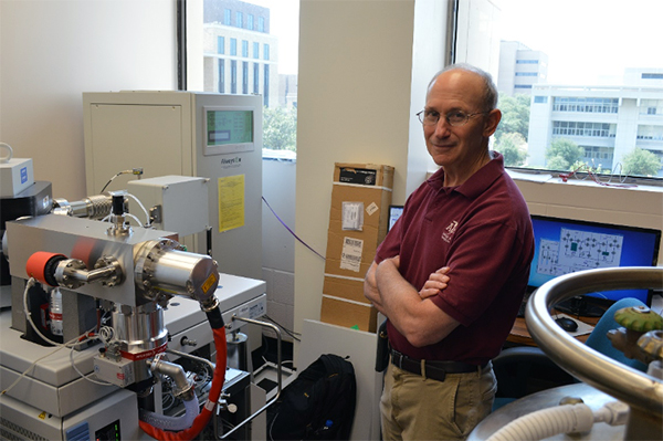 Texas A&amp;M geologist Ethan Grossman stands next to a mass spectrometer in his laboratory on the Texas A&amp;M University campus