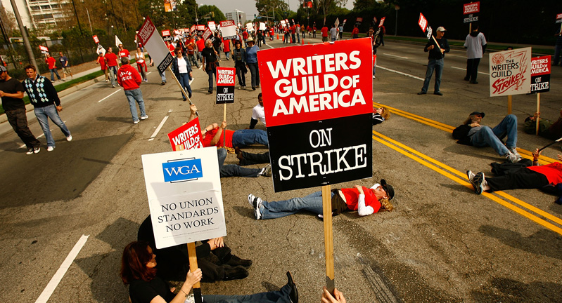 Writers Guild of America members and supporters, who are pictured standing, walking and lying down on a city street while holding protest signs in solidarity with the current writers' strike