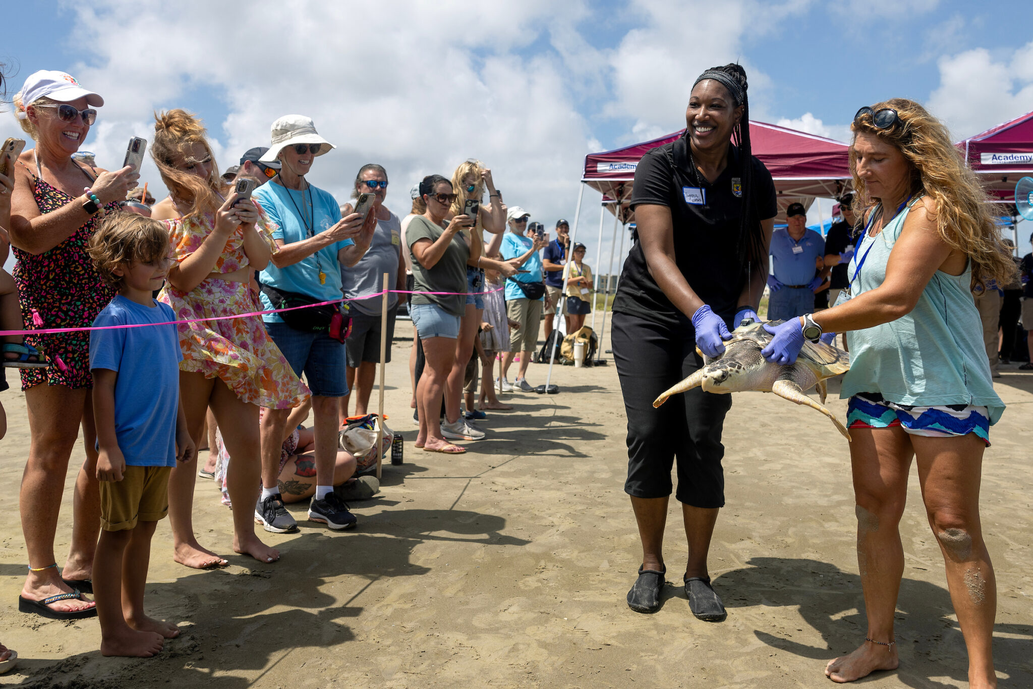 U.S. Fish and Wildlife Service Senior Biologist Syrena Johnson carries Tally the sea turtle down the beach alongside Frankie Hobro, director and owner of the Anglesey Sea Zoo in Wales as a crowd of spectators watch, smiling and in some cases documenting with their cell phones
