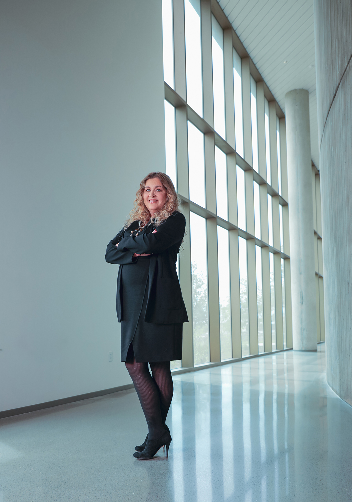 Texas A&amp;M chemist Karen Wooley smiles for the camera, arms folded across her chest and standing in a hallway bathed in natural light from a bank of floor-to-ceiling windows