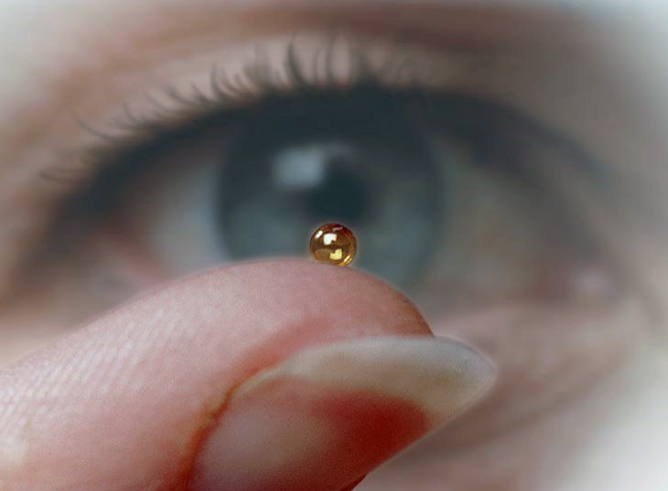 Close-up of an inertial confinement fusion fuel microcapsule, positioned on a fingertip and being scrutinized by a human eye in the background