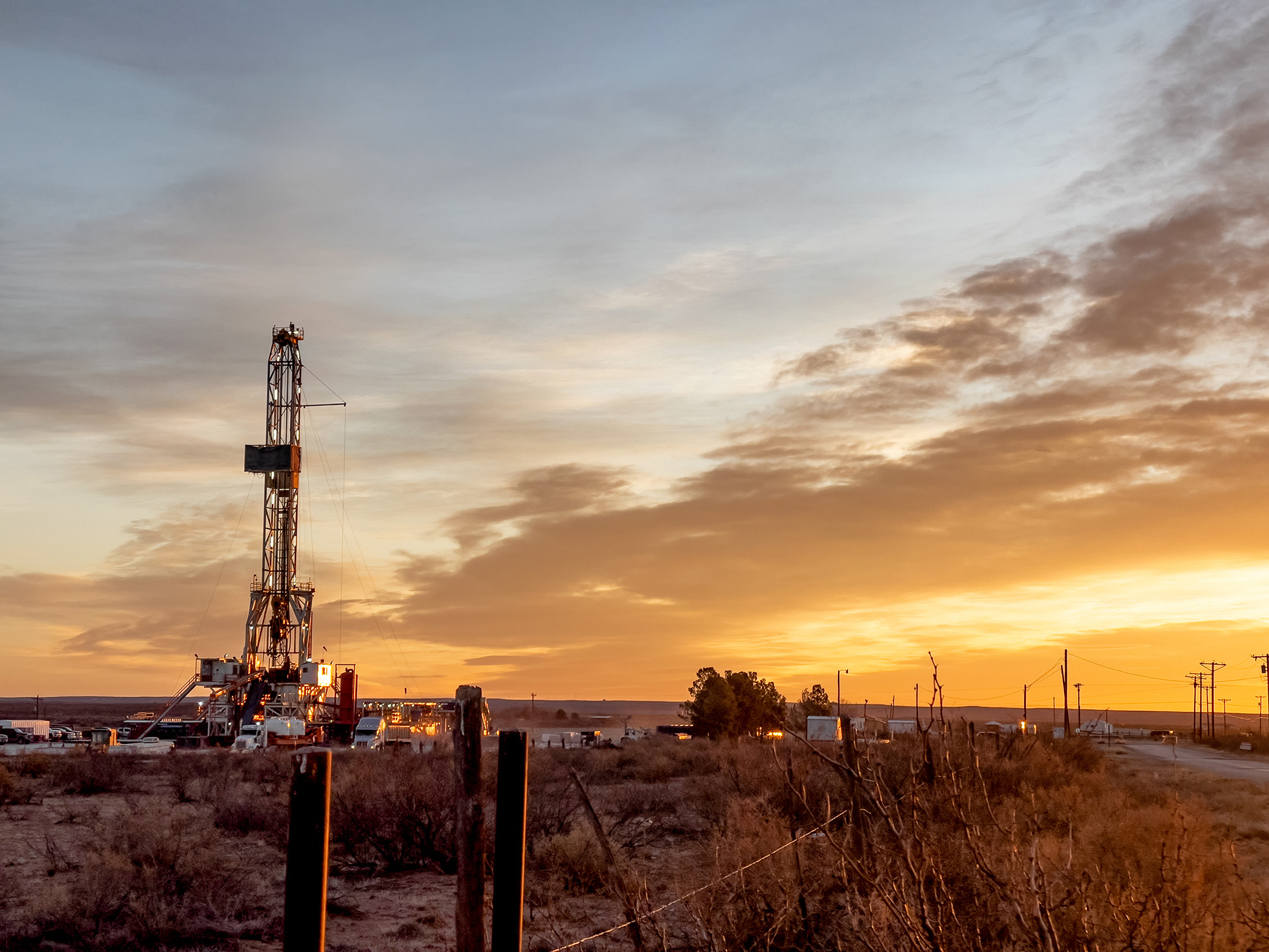 Drone view of an oil or gas drill fracking rig pad in New Mexico with the sunset in the background