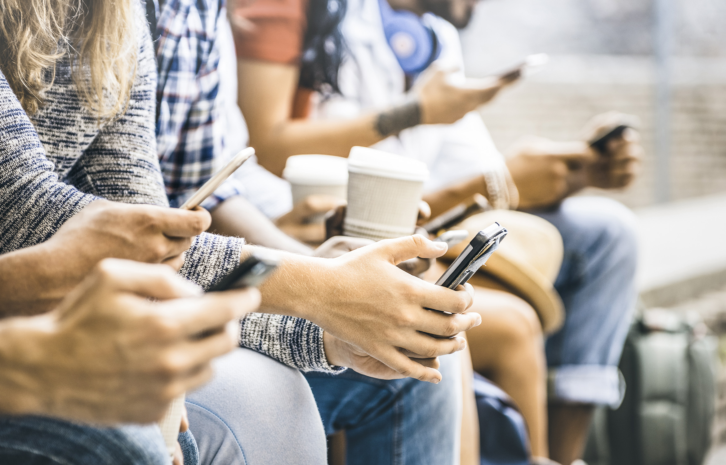 Group of college-aged students seated in a group using smartphones and holding coffee cups
