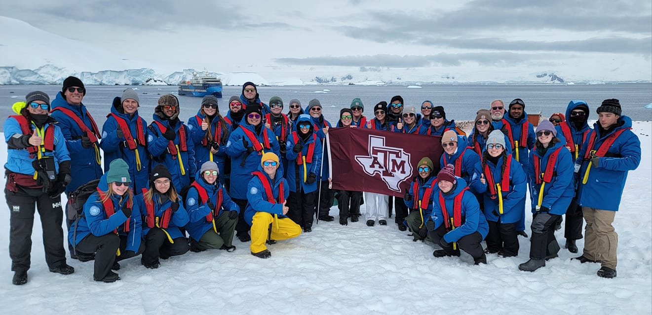 Students, faculty and staff who participated in Texas A&M University's first study abroad trip to Antarctica in late fall 2023 pose with a maroon Texas A&M flag