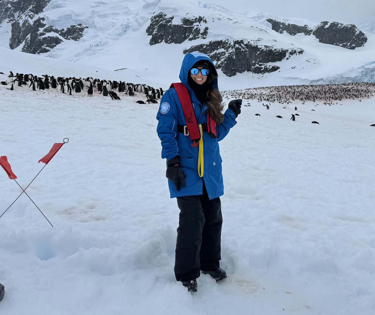 Veterinary graduate student Mary Chandra smiles against a backdrop of snow-covered mountains while pointing to a group of penguins gathered behind her during Texas A&amp;M University's first study abroad trip to Antarctica in late fall 2023