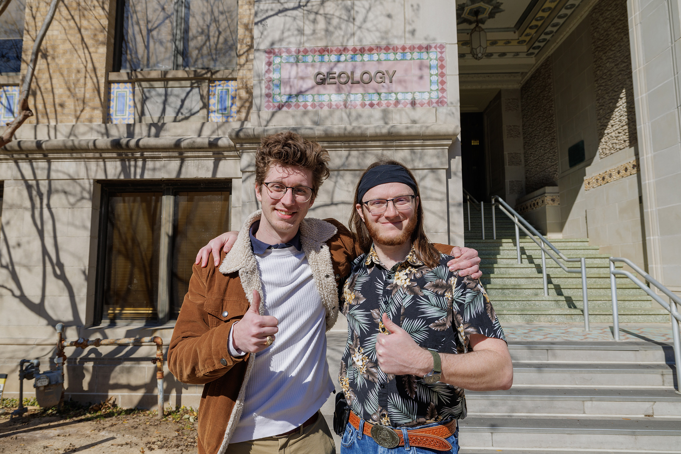 Texas A&amp;M University geology graduate students Dirk van de Laar and Reid "Zeke" Buskirk pose arm in arm while flashing thumbs up signs outside the Halbouty Geosciences Building on the Texas A&amp;M campus