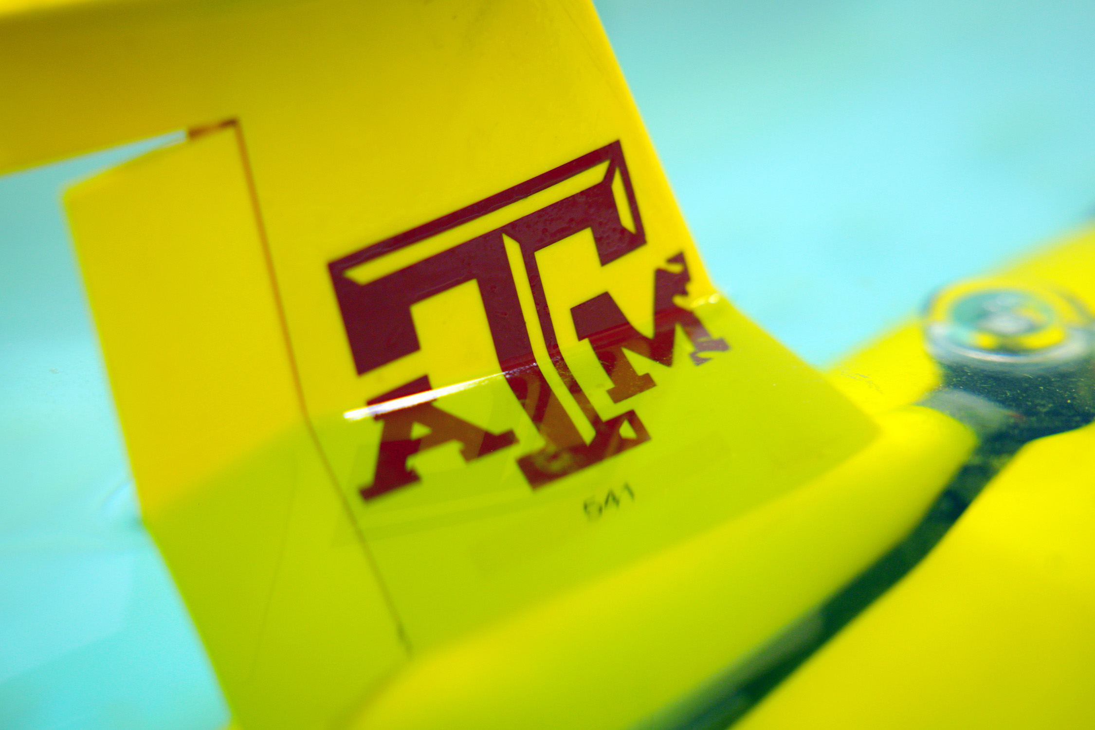 A yellow glider featuring a maroon Texas A&amp;M University logo floats in a pool of water within a Geochemical and Environmental Research Group laboratory